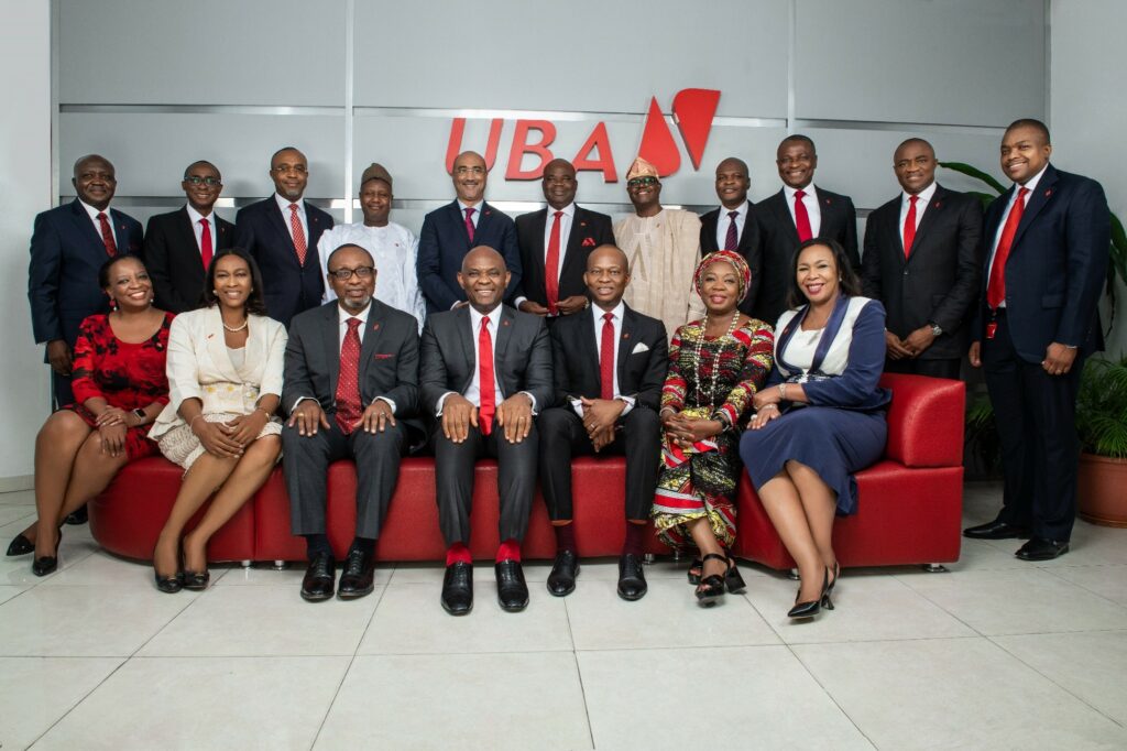 Leadership team of UBA, dressed formally with men in red ties and women in dresses against a gray background